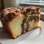 A close-up slice of moist sour cream coffee cake featuring a cinnamon swirl and thick streusel topping.