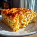 A thick, golden slice of southern baked macaroni and cheese with a bubbly, browned top served on a white plate.
