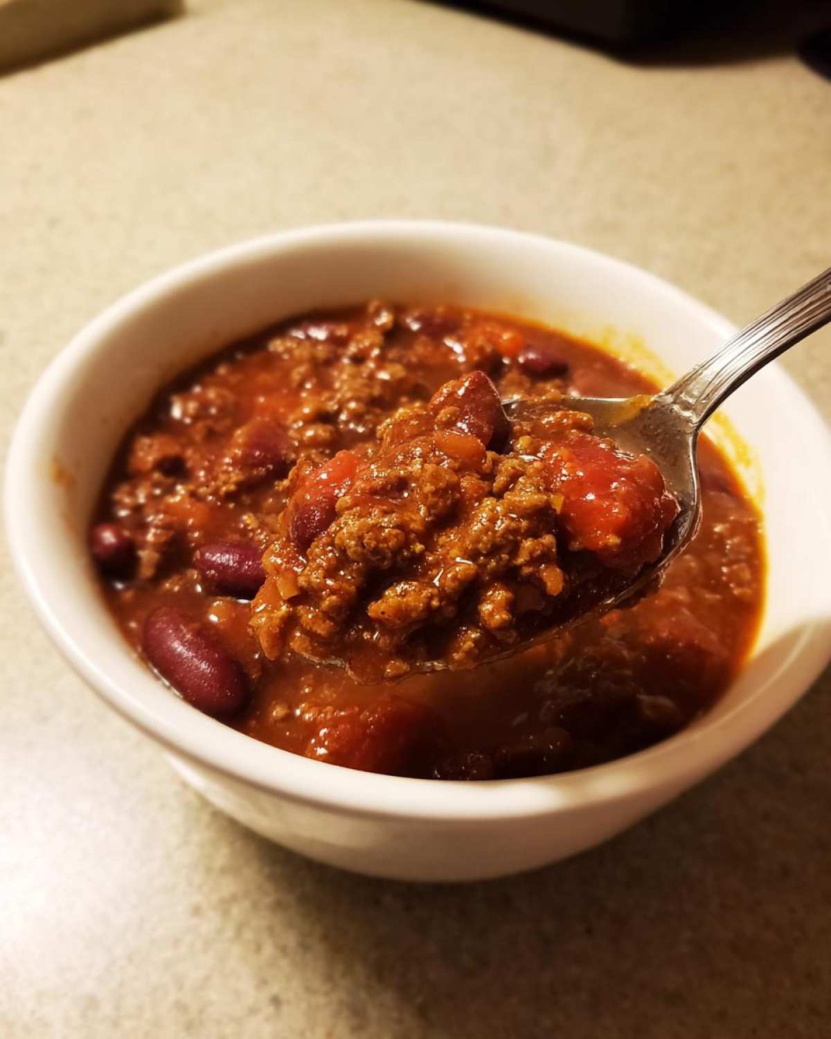 A spoonful of hearty, bean-filled crockpot chili being lifted from a white bowl.