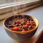 Close-up of a steaming bowl of rich, dark black bean chili with visible chunks of tomato.