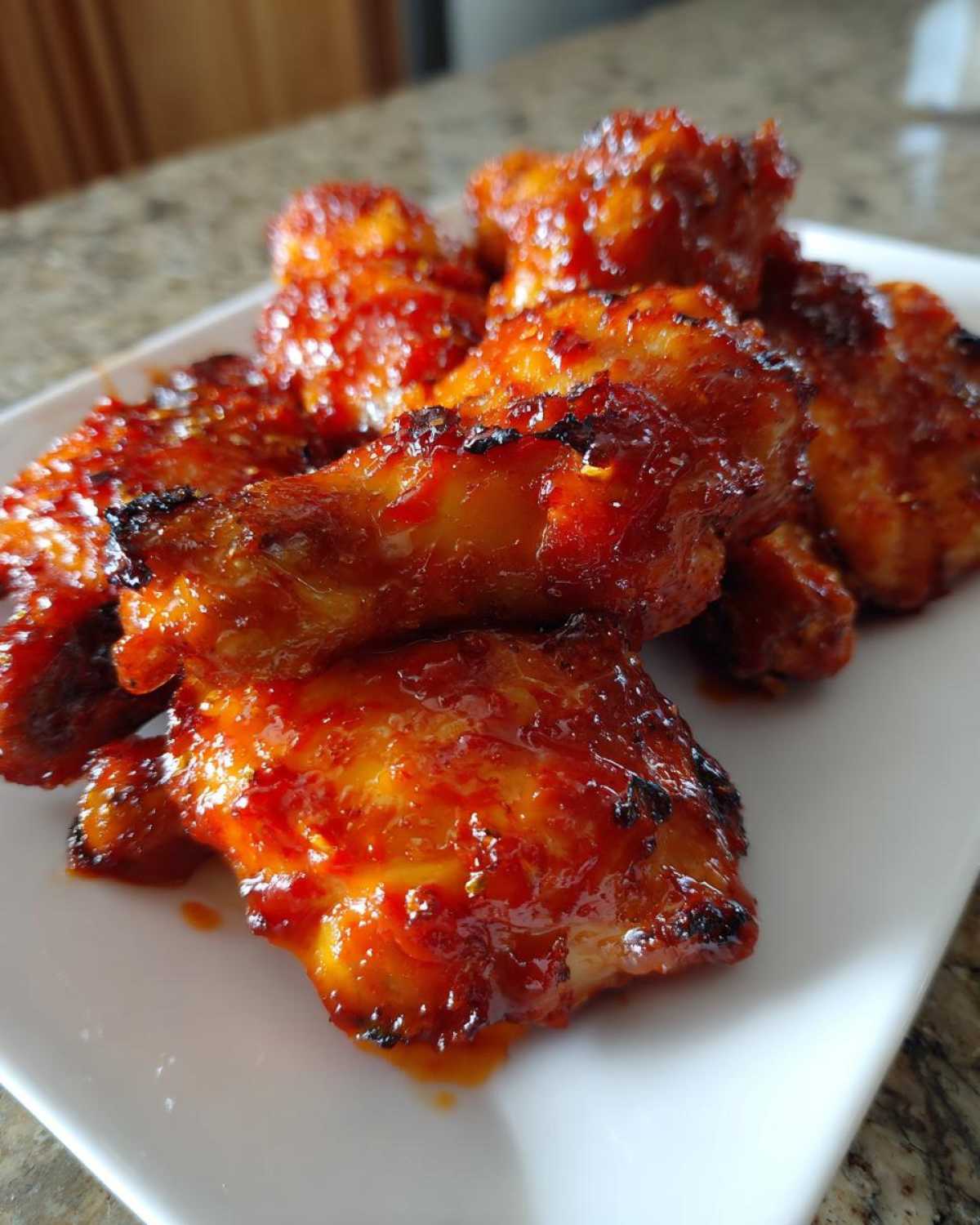 Close-up of several sticky, glazed gochujang chicken wings piled on a white plate.
