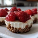 Close-up of several individual strawberry cheesecake bites with graham cracker crusts sitting on a white rectangular plate.