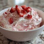 A white bowl filled with creamy, swirled strawberry cheesecake dip topped with fresh diced strawberries.