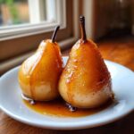 Two perfectly cooked poached pears glistening with a rich, amber syrup on a white plate.