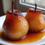 Two glistening, caramelized poached pears sitting in a pool of amber syrup on a white plate.