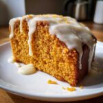 A moist slice of orange sweet potato pound cake topped with thick white glaze and zest.