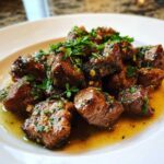 Close-up of tender crockpot steak bites coated in a rich, buttery garlic sauce and topped with fresh parsley.