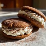 Close-up of two decadent tiramisu cookies filled with white cream and dusted with cocoa powder.