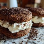 Two decadent tiramisu cookies filled with whipped cream and dusted with cocoa powder.