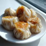 Close-up of five pan-fried Traditional Chinese Dumplings with golden-brown bottoms served on a white plate.