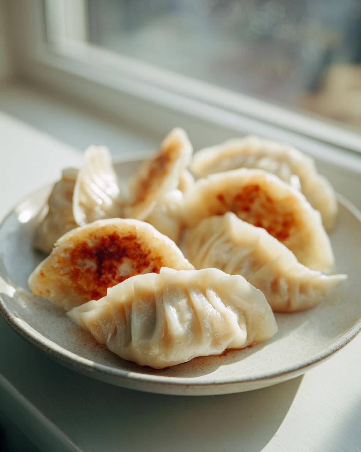 A plate of freshly cooked Traditional Chinese Dumplings, some showing golden-brown pan-fried bottoms.
