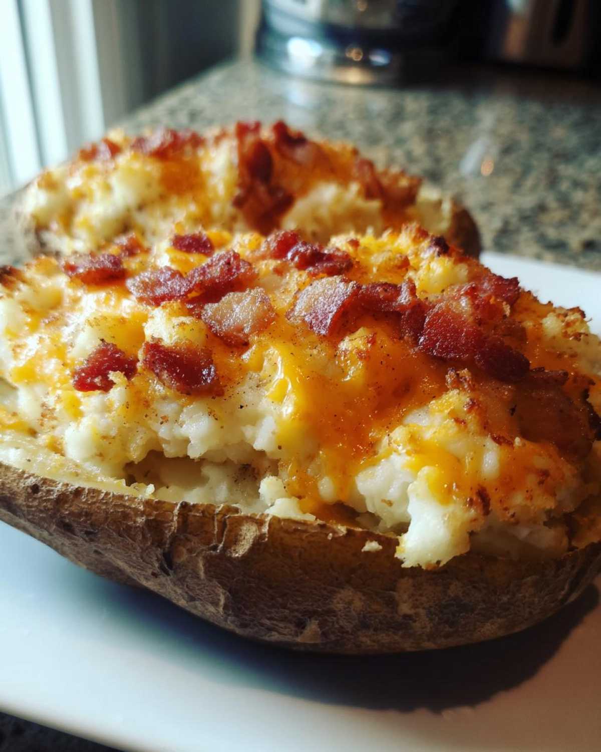 Close-up of a twice baked potato stuffed with creamy filling, melted cheddar cheese, and crispy bacon bits.