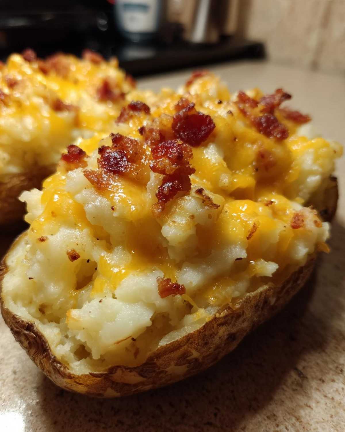 A close-up of a twice baked potato stuffed with mashed potato, melted cheddar cheese, and topped with crispy bacon bits.