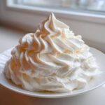 A beautiful mound of fluffy, white vanilla buttercream frosting piped high on a white plate.