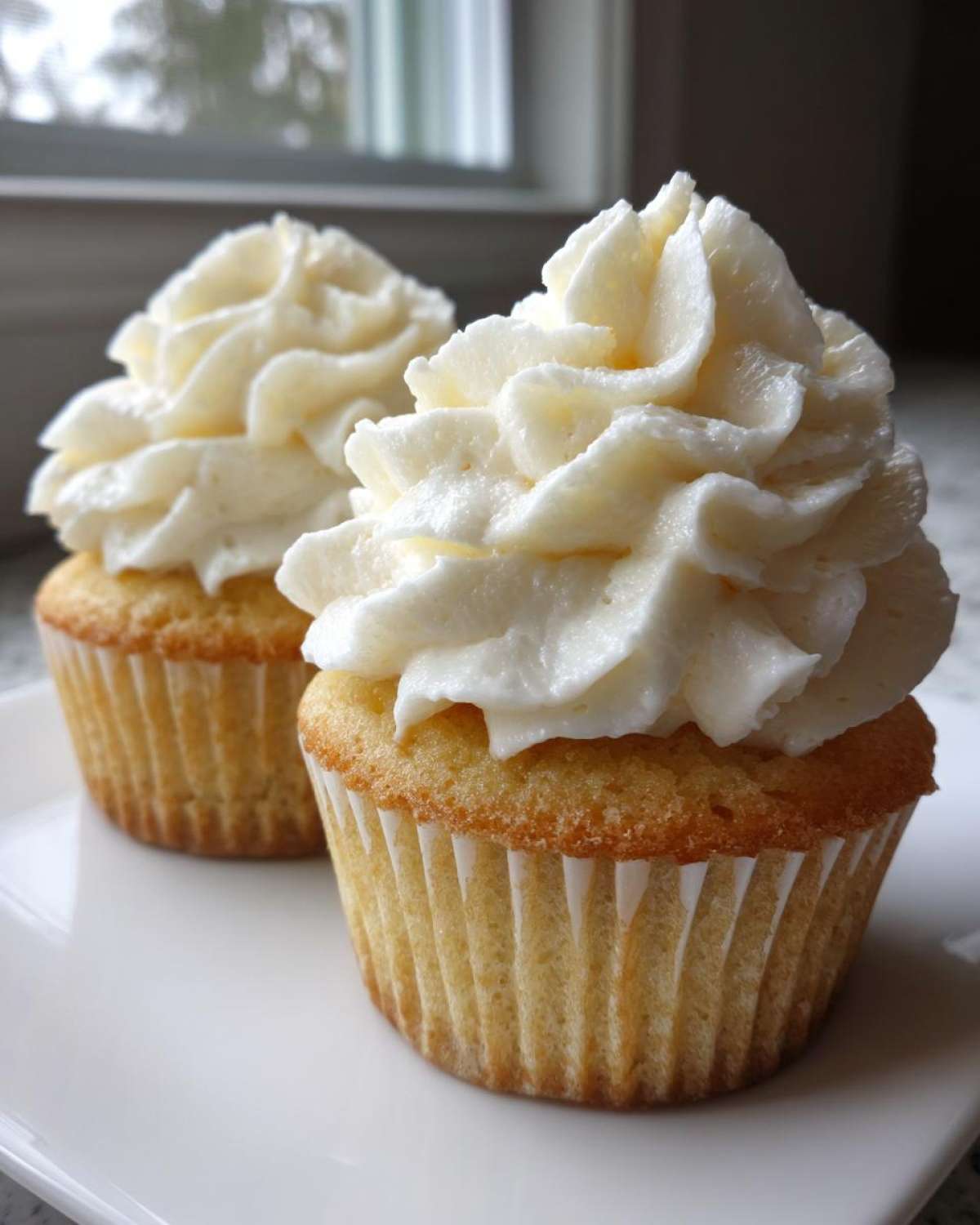 Close-up of two delicious vanilla cupcakes topped with high swirls of white vanilla buttercream frosting.
