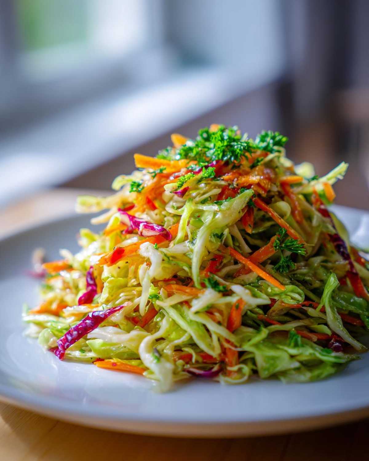 A vibrant mound of fresh cabbage salad featuring shredded green and red cabbage and carrots, topped with parsley.