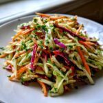 A mound of fresh, colorful cabbage salad featuring shredded green and red cabbage, carrots, and chopped parsley.