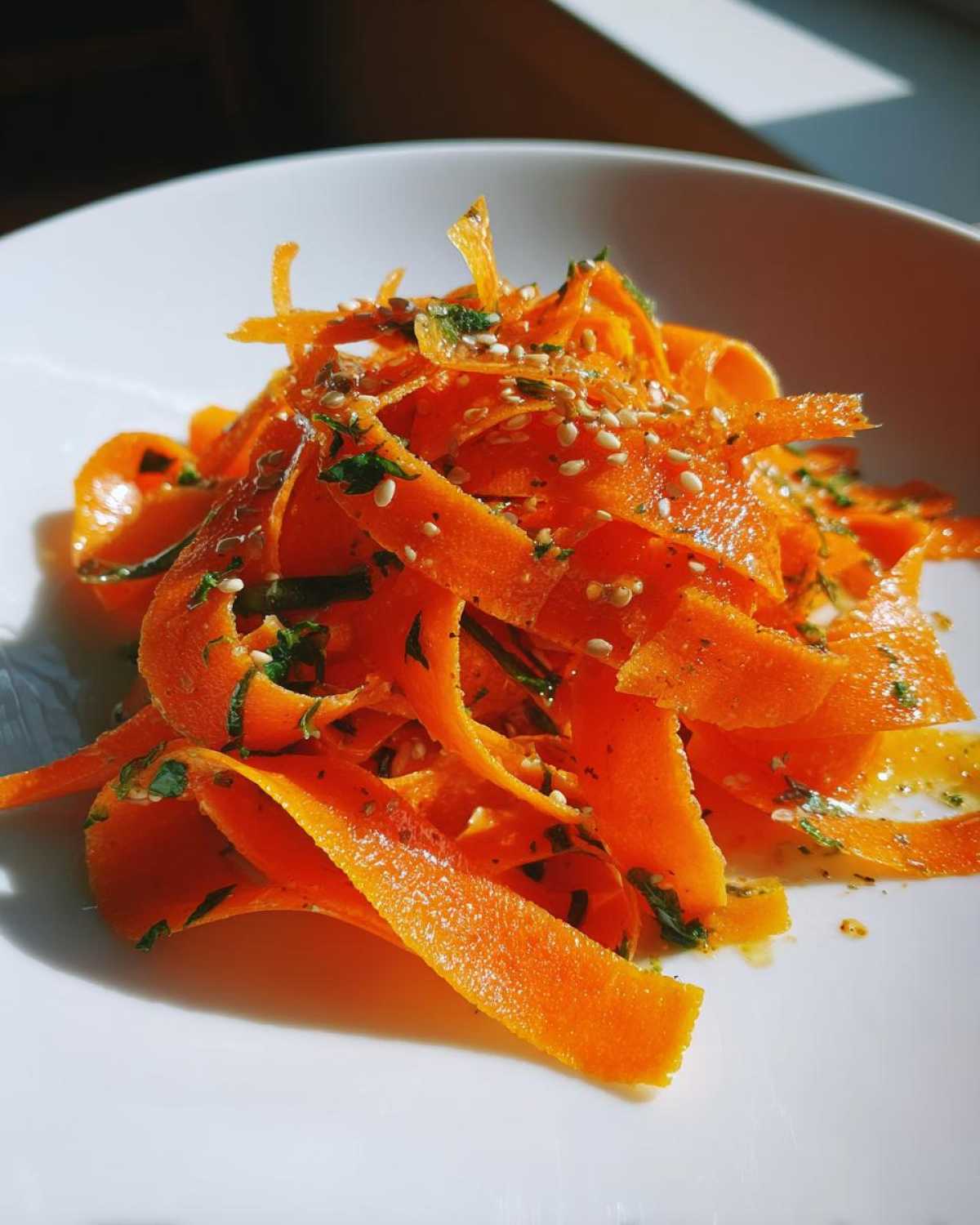 Close-up of vibrant orange ribbons in a raw carrot salad, topped with sesame seeds and herbs.