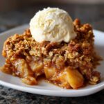 Close-up of a warm serving of apple crisp with a scoop of vanilla ice cream melting on top.