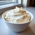 A white bowl filled with fluffy, freshly whipped cream, perfect for a quick fruit dip.