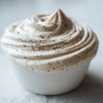 Close-up of a swirl of light beige, creamy homemade cream of chicken soup, topped with black pepper flecks.