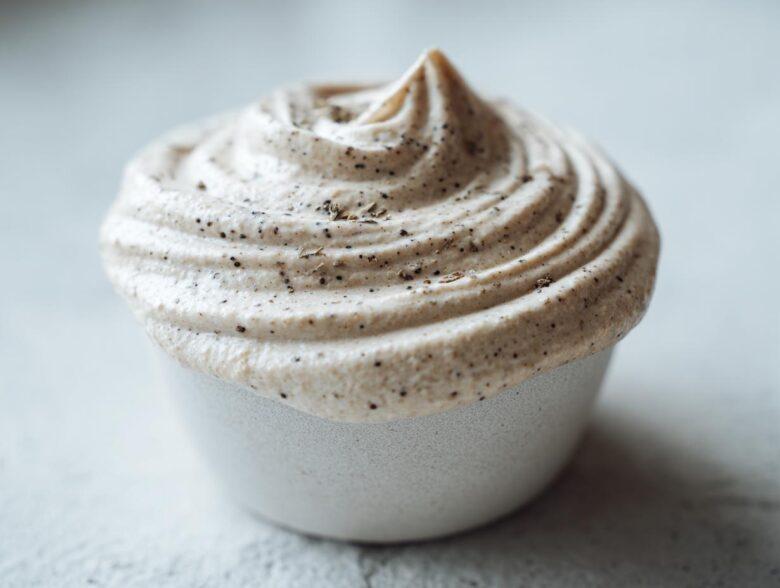 Close-up of a swirl of light beige, creamy homemade cream of chicken soup, topped with black pepper flecks.