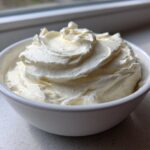 A close-up of fluffy, whipped white fruit dip swirled high in a small white bowl.