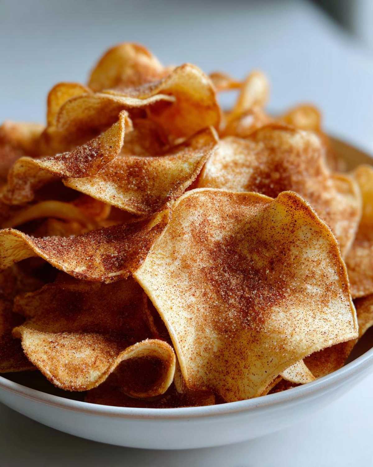 Close-up of crispy Air Fryer Cinnamon Sugar Apple Chips piled high in a light-colored bowl.