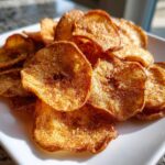 A close-up of crispy, golden Air Fryer Cinnamon Sugar Apple Chips piled high on a white plate.