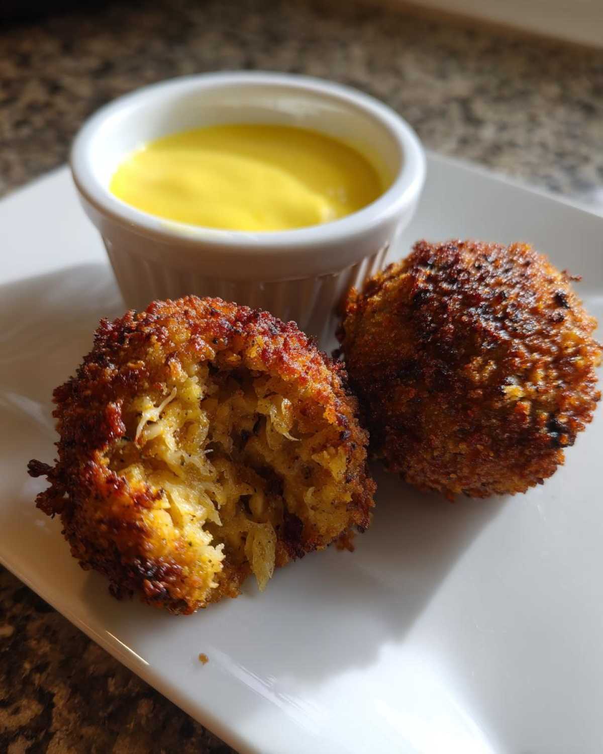 Two golden brown Air Fryer Crispy Crab Cakes served with a side of bright yellow lemon aioli dipping sauce.