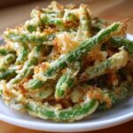A close-up of a pile of Air Fryer Crispy Tempura Green Beans on a white plate.