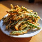 A pile of golden brown Air Fryer Crispy Tempura Green Beans served on a white plate.