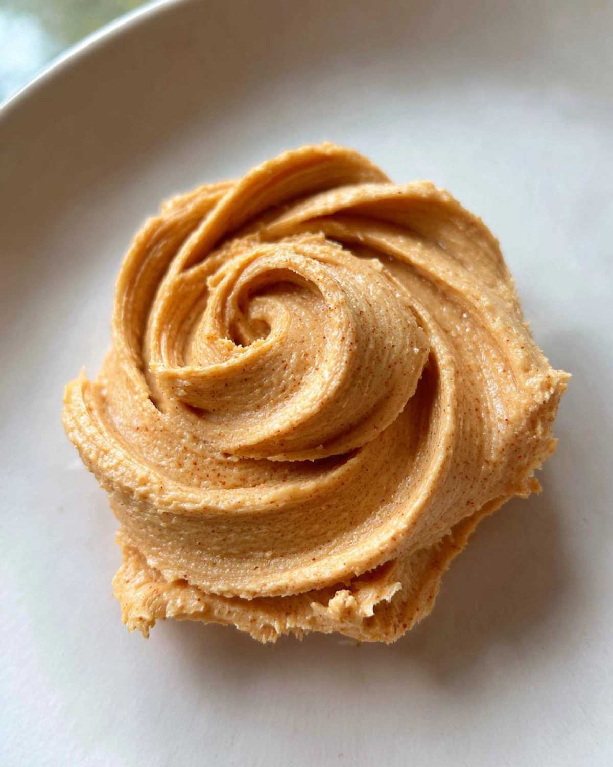 Close-up of Copycat Texas Roadhouse Cinnamon Honey Butter piped into a rosette shape on a white plate.