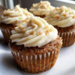 Close-up of a moist Gluten-Free Carrot Cake Cupcake topped with thick, swirled cream cheese frosting and carrot shavings.