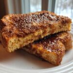 Two slices of thick Gluten-Free Cinnamon Crunch French Toast stacked on a white plate.