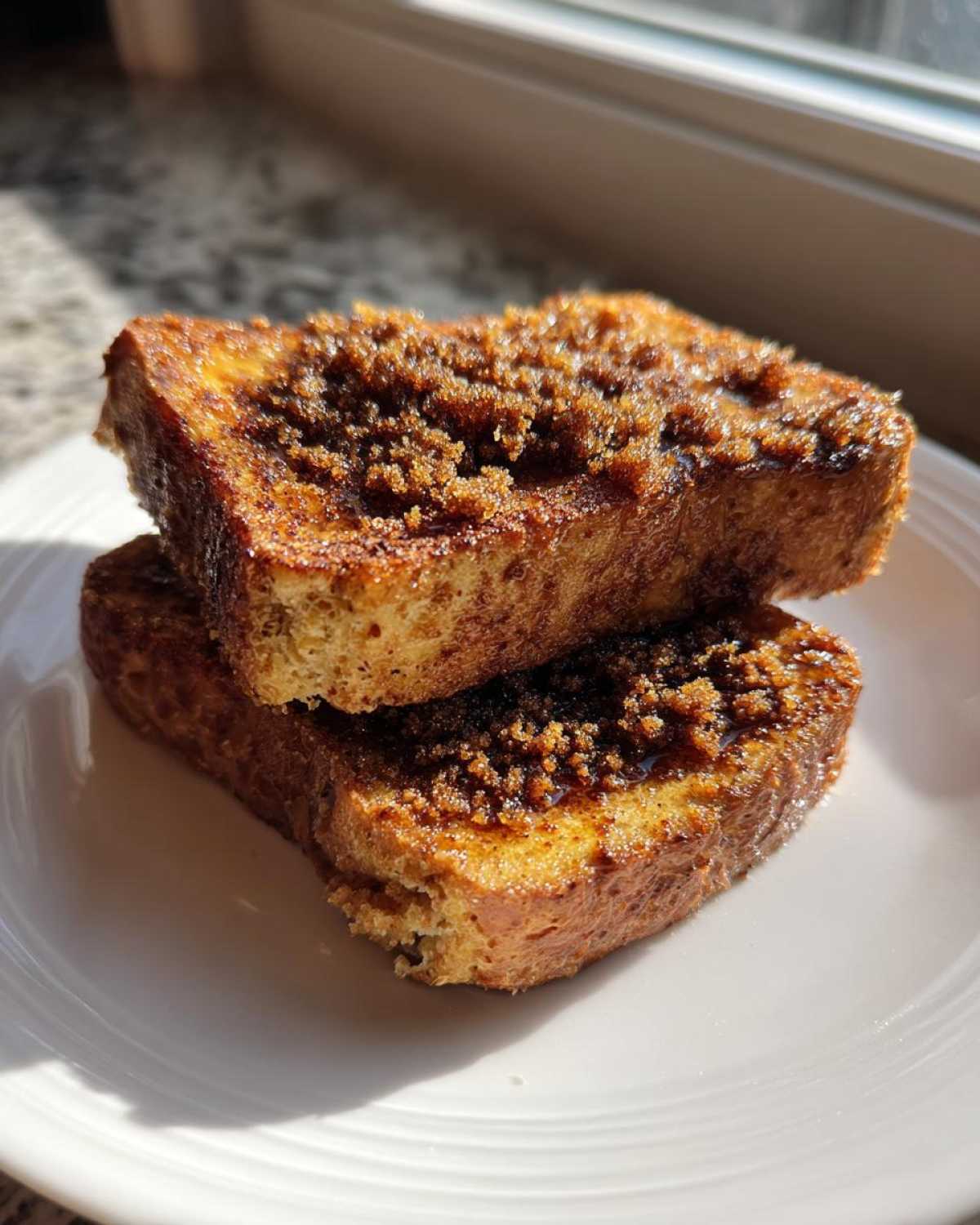 Two slices of Gluten-Free Cinnamon Crunch French Toast stacked on a white plate with brown sugar topping.