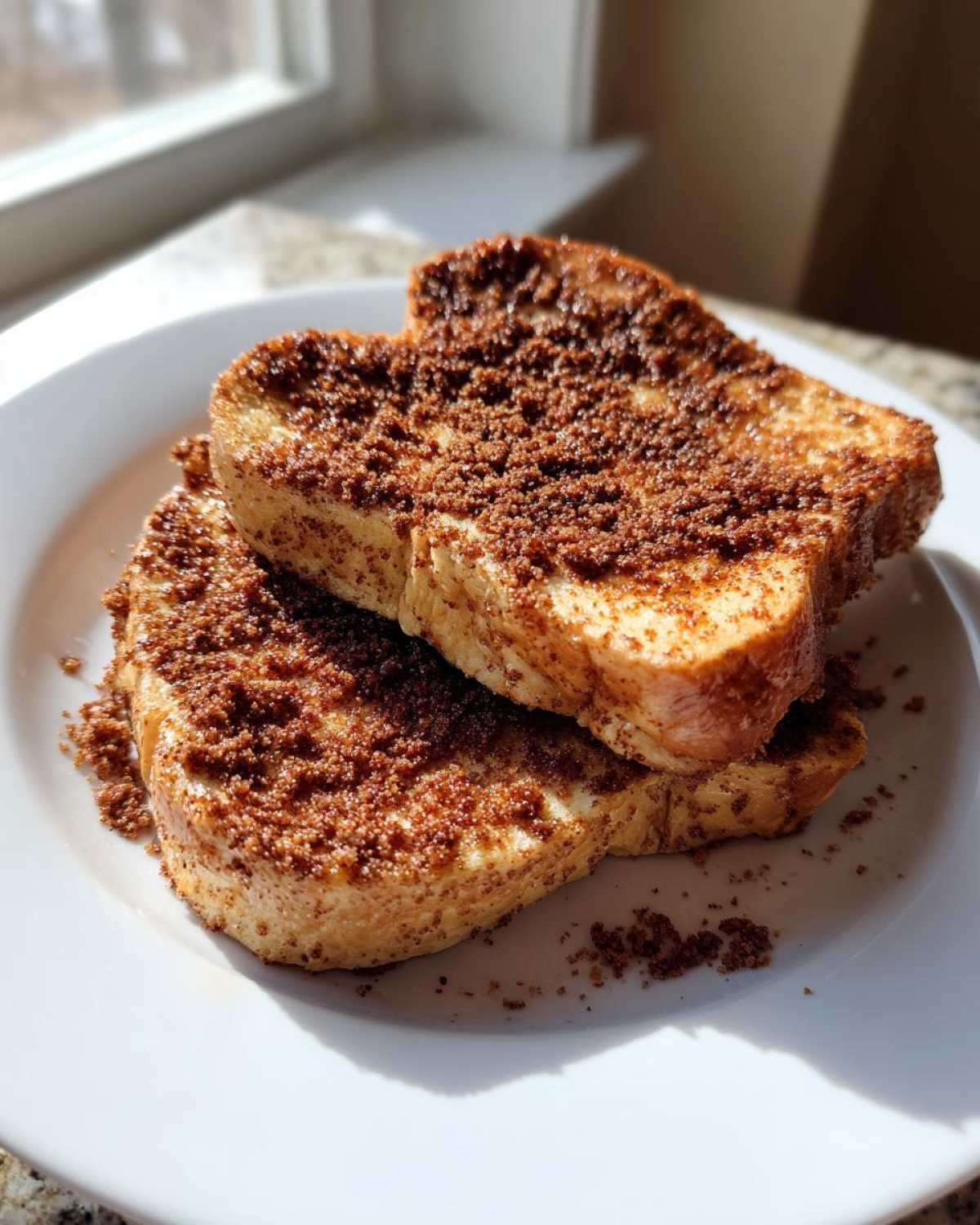 Two slices of Gluten-Free Cinnamon Crunch French Toast stacked on a white plate, heavily topped with cinnamon sugar.