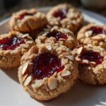 Close-up of several Gluten-Free Raspberry Almond Thumbprint Cookies topped with jam and sliced almonds.