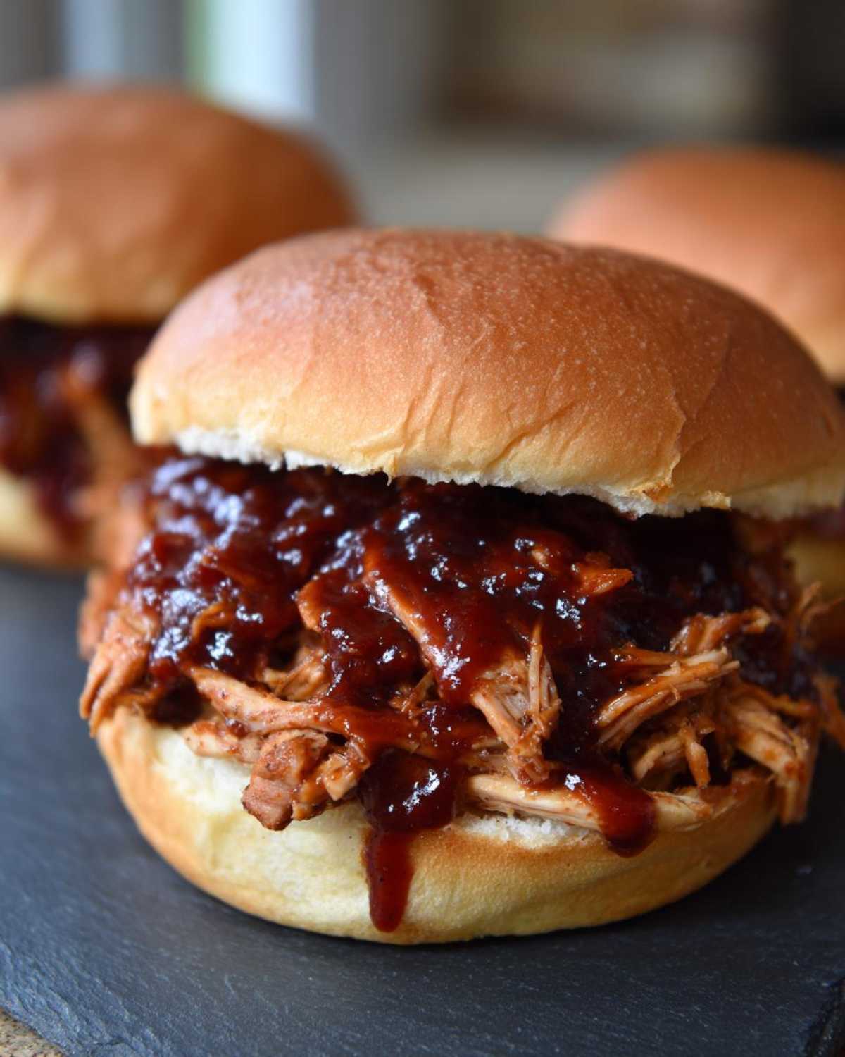 A close-up of a juicy Instant Pot BBQ Pulled Chicken Sandwich piled high with shredded meat and dripping BBQ sauce on a soft bun.