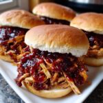 Close-up of four Instant Pot BBQ Pulled Chicken Sandwiches piled high with shredded chicken and sauce on soft buns.