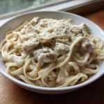 A white bowl filled with Instant Pot Creamy Chicken Alfredo Pasta, topped with grated Parmesan cheese.