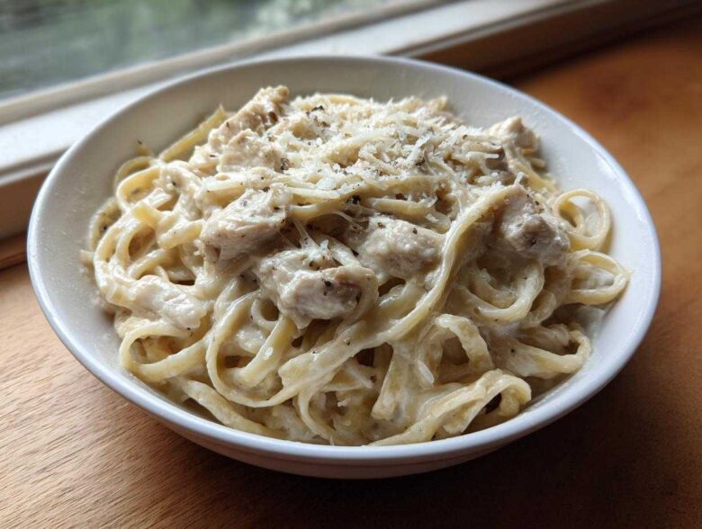 A white bowl filled with Instant Pot Creamy Chicken Alfredo Pasta, topped with grated Parmesan cheese.