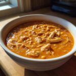 Close-up of a white bowl filled with rich, orange Instant Pot Creamy Chicken Taco Soup topped with shredded chicken and corn.