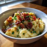 A white bowl filled with Instant Pot Creamy Potato Soup with Bacon crumbles and fresh chives.
