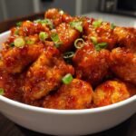 Close-up of sticky, glazed Instant Pot Honey Sriracha Chicken pieces topped with sliced green onions in a white bowl.