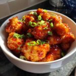 Close-up of crispy chicken pieces coated in a glossy red sauce, garnished with sliced green onions, representing Instant Pot Honey Sriracha Chicken.