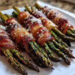 Close-up of crispy Keto Bacon Wrapped Asparagus Bundles sprinkled with Parmesan cheese on a white plate.