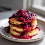 Stack of three fluffy Keto Coconut Flour Pancakes topped with rich, dark berry sauce.
