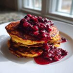 Stack of fluffy Keto Coconut Flour Pancakes topped with rich, dark berry sauce.