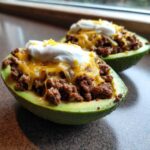 Two halves of Keto Taco Stuffed Avocados filled with seasoned ground beef, melted cheese, and sour cream.